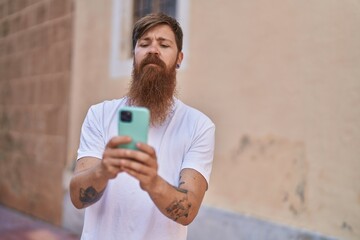 Wall Mural - Young redhead man using smartphone with relaxed expression at street