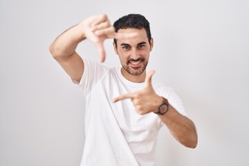 Sticker - Handsome hispanic man standing over white background smiling making frame with hands and fingers with happy face. creativity and photography concept.