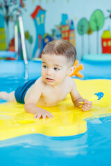 Wall Mural - Little cheerful 2-year-old boy is learning to swim in the pool. Swimming lessons for children. Swimming school for children.