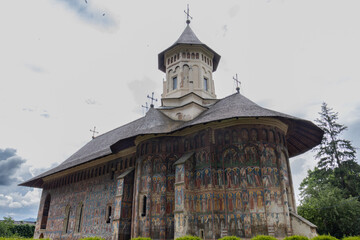 Beautiful facade of a painted monastery in Romania with dramatic sky background