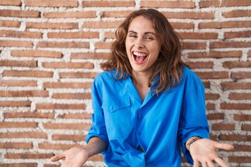 Sticker - Beautiful brunette woman standing over bricks wall smiling cheerful with open arms as friendly welcome, positive and confident greetings