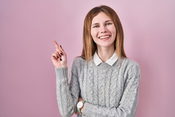 Sticker - Beautiful woman standing over pink background with a big smile on face, pointing with hand finger to the side looking at the camera.