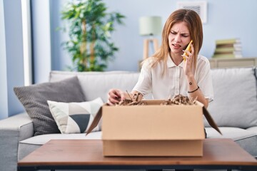 Poster - Young blonde woman speaking on the phone unpacking cardboard box at home