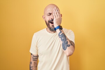 Wall Mural - Hispanic man with tattoos standing over yellow background yawning tired covering half face, eye and mouth with hand. face hurts in pain.