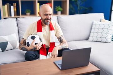 Sticker - Hispanic man with tattoos watching football match hooligan holding ball on the laptop looking positive and happy standing and smiling with a confident smile showing teeth