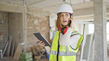 Poster - Young blonde woman architect talking on smartphone looking touchpad at construction site