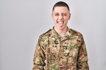 Wall Mural - Young man wearing camouflage army uniform sticking tongue out happy with funny expression. emotion concept.