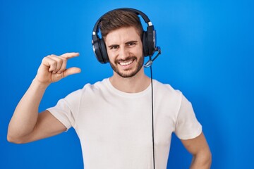 Poster - Hispanic man with beard listening to music wearing headphones smiling and confident gesturing with hand doing small size sign with fingers looking and the camera. measure concept.