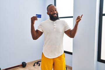 Poster - African american man wearing sportswear holding credit card smiling happy pointing with hand and finger to the side