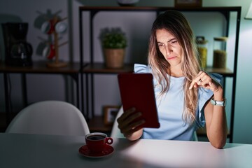 Sticker - Young hispanic woman using touchpad sitting on the table at night pointing down looking sad and upset, indicating direction with fingers, unhappy and depressed.