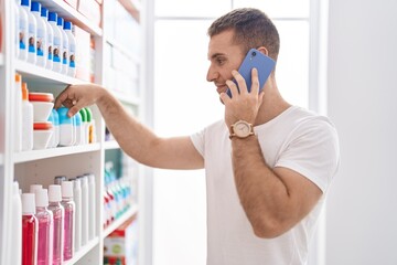 Wall Mural - Young caucasian man customer talking on smartphone holding deodorant at pharmacy