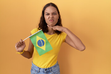 Poster - Young hispanic woman holding brazil flag cutting throat with hand as knife, threaten aggression with furious violence