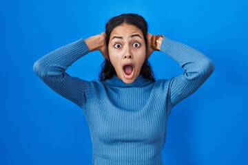 Poster - Young brazilian woman standing over blue isolated background crazy and scared with hands on head, afraid and surprised of shock with open mouth