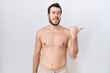 © Krakenimages.com - Young hispanic man standing shirtless over white background smiling with happy face looking and pointing to the side with thumb up.