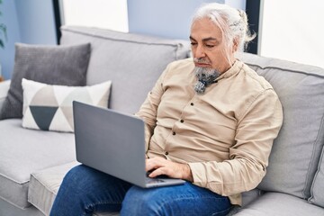 Wall Mural - Middle age grey-haired man using laptop sitting on sofa at home