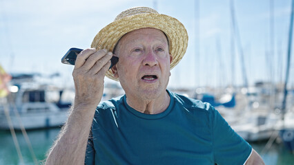 Poster - Senior grey-haired man tourist wearing summer hat listening voice message by smartphone at port