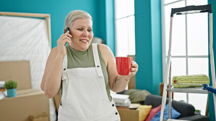 Poster - Middle age grey-haired woman talking on smartphone drinking coffee at new home