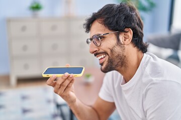 Sticker - Young hispanic man talking on the smartphone sitting on sofa at home