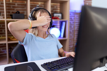 Canvas Print - Young caucasian woman playing video games wearing headphones smiling and laughing with hand on face covering eyes for surprise. blind concept.