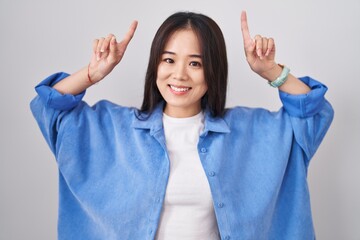 Sticker - Young chinese woman standing over white background smiling amazed and surprised and pointing up with fingers and raised arms.