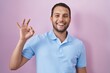 Hispanic man standing over pink background smiling positive doing ok sign with hand and fingers. successful expression.