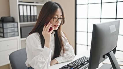 Canvas Print - Young chinese woman business worker using computer talking on smartphone at office