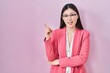 © Krakenimages.com - Chinese business young woman wearing glasses with a big smile on face, pointing with hand and finger to the side looking at the camera.