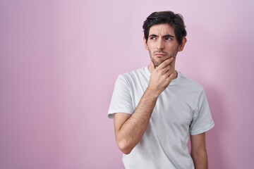 Wall Mural - Young hispanic man standing over pink background thinking worried about a question, concerned and nervous with hand on chin