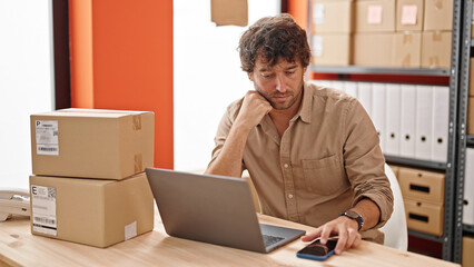 Canvas Print - Young hispanic man ecommerce business worker using laptop and smartphone at office