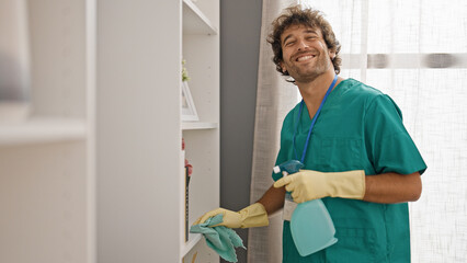 Wall Mural - Young hispanic man cleaning shelving with a cloth smiling at home