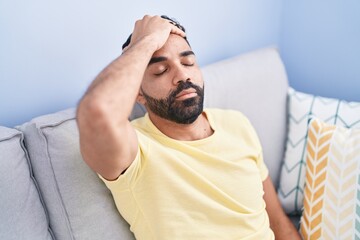 Sticker - Young arab man relaxed with hand on head sitting on sofa at home