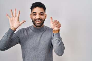 Sticker - Hispanic man with beard standing over white background showing and pointing up with fingers number six while smiling confident and happy.