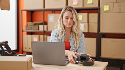 Poster - Young blonde woman ecommerce business worker using laptop holding headphones at office