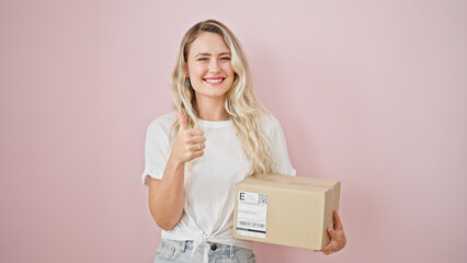 Poster - Young blonde woman smiling confident holding package doing thumb up gesture over isolated pink background