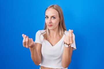 Poster - Young caucasian woman standing over blue background doing money gesture with hands, asking for salary payment, millionaire business