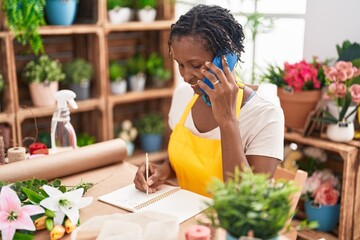 Canvas Print - Middle age african american woman florist talking on smartphone writing on notebook at flower shop