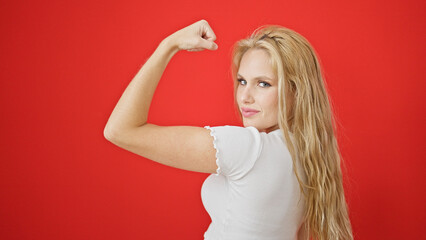 Wall Mural - Young blonde woman smiling confident doing strong gesture with arm over isolated red background