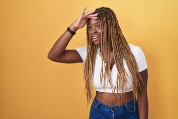 Sticker - African american woman with braided hair standing over yellow background very happy and smiling looking far away with hand over head. searching concept.