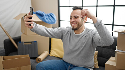 Canvas Print - Hispanic man doing video call sitting on the sofa showing keys at new home