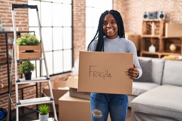 Wall Mural - African american woman smiling confident holding fragile package at new home