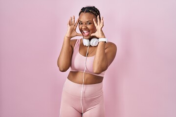 Canvas Print - African american woman with braids wearing sportswear and headphones smiling cheerful playing peek a boo with hands showing face. surprised and exited