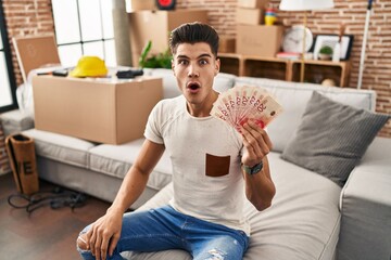 Poster - Young hispanic man moving to a new home holding shekels scared and amazed with open mouth for surprise, disbelief face