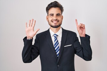 Poster - Young hispanic man with tattoos wearing business suit and tie showing and pointing up with fingers number six while smiling confident and happy.