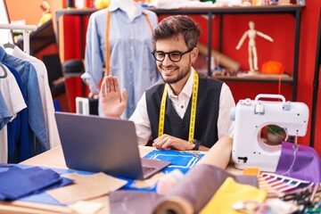 Sticker - Young hispanic man with tattoos dressmaker designer using laptop at tailor room looking positive and happy standing and smiling with a confident smile showing teeth