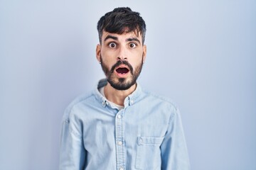 Wall Mural - Young hispanic man with beard standing over blue background afraid and shocked with surprise and amazed expression, fear and excited face.