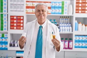 Poster - Middle age grey-haired man pharmacist smiling confident holding pills bottles at pharmacy