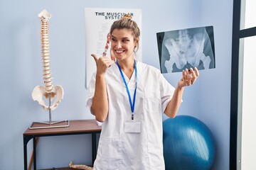 Canvas Print - Young woman holding pelvis radiography pointing thumb up to the side smiling happy with open mouth