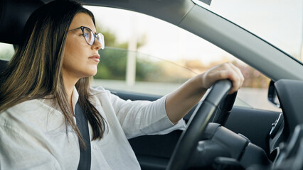 Young beautiful hispanic woman driving a car wearing glasses on the road