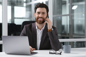 Poster - Man talking on phone while working with laptop at white desk in office