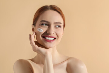 Poster - Beautiful young woman with sun protection cream on her face against beige background, space for text